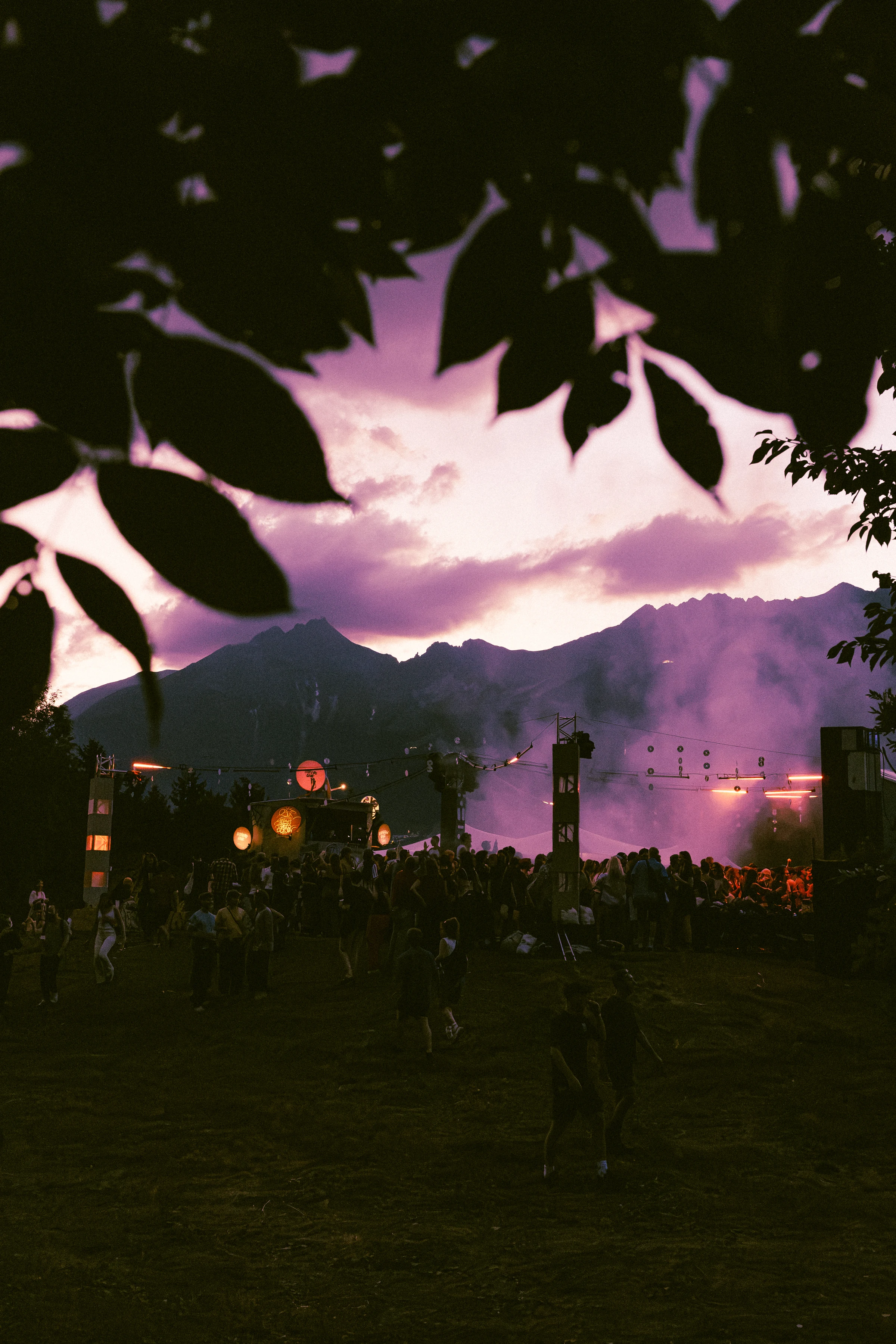 Abendlicht über dem Festivalgelände: Berge, tanzende Menschen und violetter Nebel am Floor.